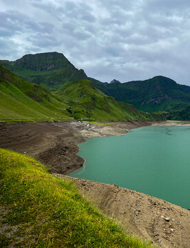 Aerial view of the turquoise lake nestled among rolling green hills and rugged mountains under a cloudy sky, Ritom lake, Quinto, Ticino, Switzerland.