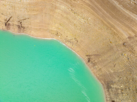 Aerial view of turquoise waters meet the rugged, earthy shoreline in a stark contrast of color and texture, Ritom lake, Quinto, Ticino, Switzerland.