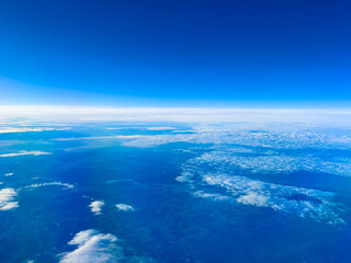 Clear skies and clouds viewed from high altitude during daytime over a vast blue landscape with no visible land during a flight