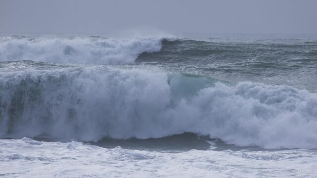 Rolling ocean swells and breaking waves under overcast sky. Natural seascape background showing rough water and sea spray.