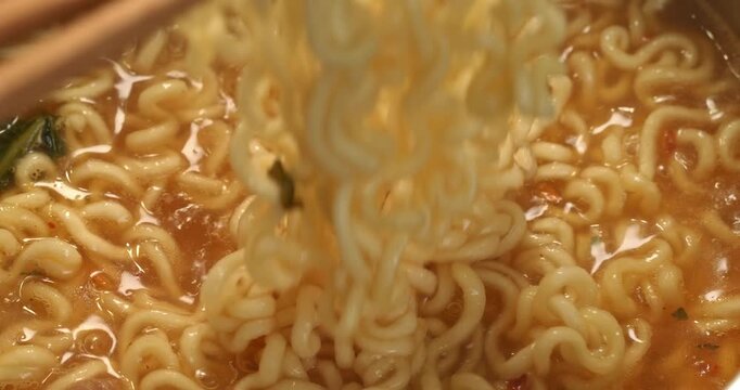Korean spicy ramyong soup with instant noodles being stirred with chopsticks, close-up footage.