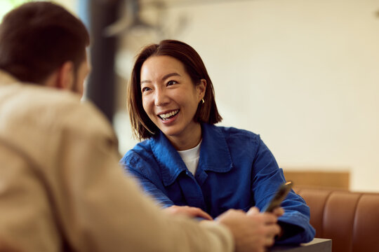 Asian Woman In Blue Shirt Enjoys Friendly Conversation At Diner With Friend