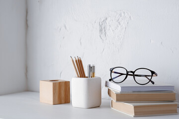 Minimalist back to school workspace with books, glasses and pencil holder on white desk, clean modern style