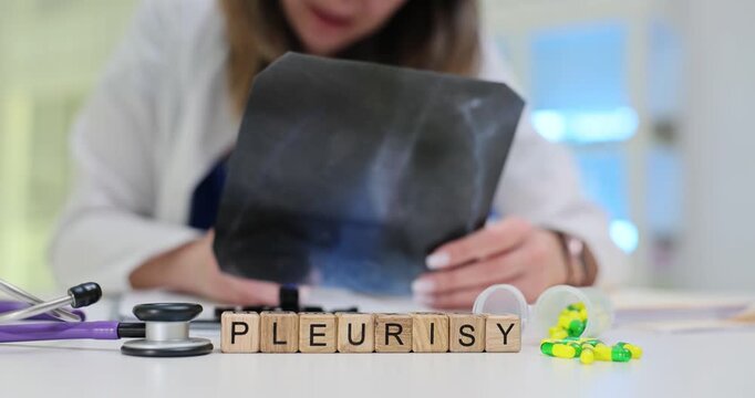 Wooden cubes spell word Pleurisy on busy medical desk. Woman doctor studies lung X-ray writing pleurisy diagnosis treatment plan carefully in hospital
