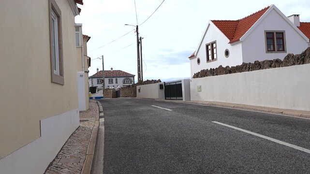 Quiet Colares street with charming Portuguese houses, red tile roofs, and calcada pavement on a calm daytime scene.