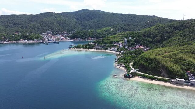 Cinematic aerial view of Romblon town and port in Romblon Philippines showing turquoise bay coastal houses beach and green hills under a clear blue sky on a sunny tropical day captured in 4K