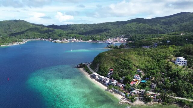 Cinematic aerial view of Romblon town and port in Romblon Philippines showing turquoise bay coastal houses beach and green hills under a clear blue sky on a sunny tropical day captured in 4K