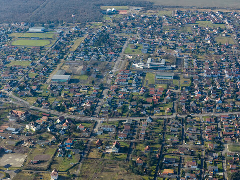 Aerial view of the town's grid-like streets, dotted with red-roofed houses and green spaces, contrasting with the dense forest edge, Wittelsheim, Grand Est, France.