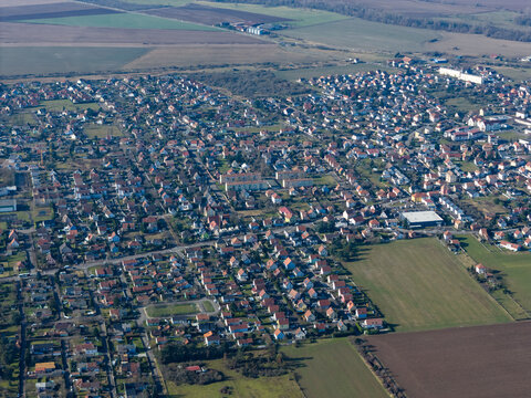 Aerial view of a sprawling townscape with rows of houses and buildings, bordered by green fields and trees, Wittelsheim, Grand Est, France.