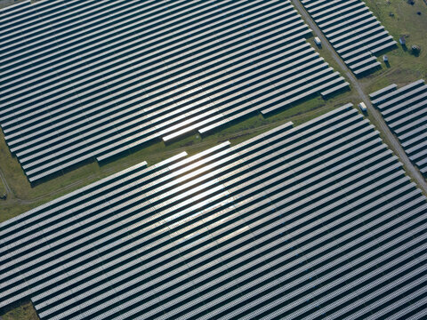 Aerial view of solar panels glinting under the sun, a sea of geometric precision contrasting with the soft green of the surrounding fields, Wittelsheim, Grand Est, France.