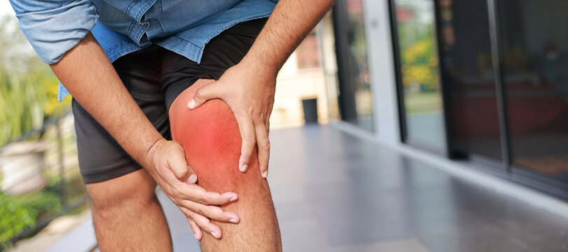 Close-up of hand holding painful injured knee with red inflamed spot and bruising. Medical concept of joint pain, arthritis, bone injury, muscle ache, or sprain in outdoor sunlight background.