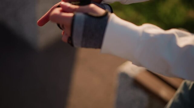 hands adjusting glove on park bench during golden afternoon, sunlight casting soft shadows, busker testing grip with guitar pick, casual hoodie outfit, focused warmup and routine before street