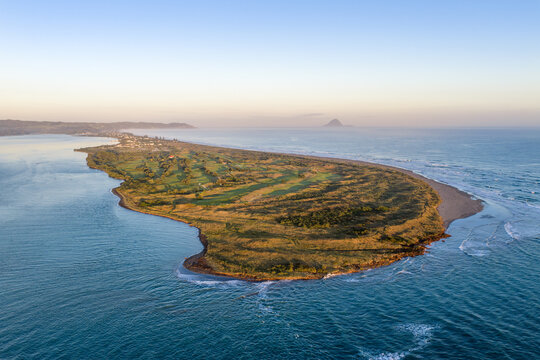 Aerial view of a lush, green peninsula embraced by the turquoise sea, contrasting with the golden coastline, Whakatane, Bay of Plenty Region, New Zealand.