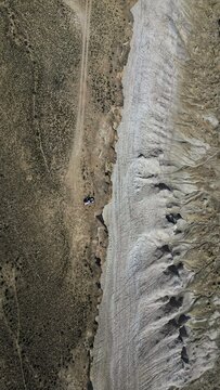 Aerial view of the stark contrast between the rugged terrain and the pale, textured earth, a solitary vehicle adding scale to the vast landscape, Say-Utes, Mangystau Region, Kazakhstan.