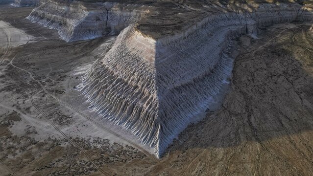 Aerial view of stark white cliffs cut through the desolate landscape, casting sharp shadows and creating a dramatic play of light and texture, Say-Utes, Mangystau Region, Kazakhstan.