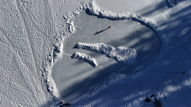 Aerial view of a person standing on a frozen pond surrounded by snow-covered landscapes, creating a stark contrast between the icy surface and the soft, powdery snow, Mesa, Colorado, United States.