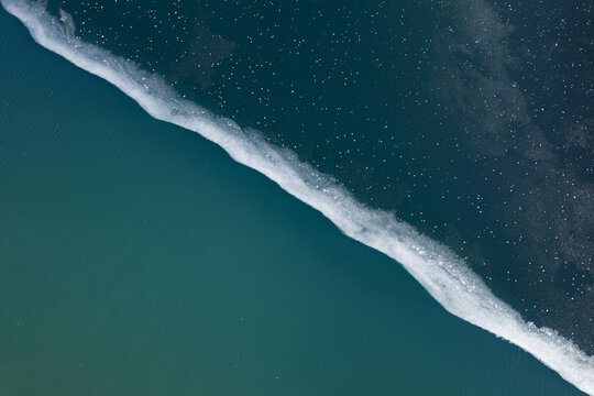 Aerial view of the contrasting dark blue and turquoise waters separated by a line of white foam, creating a stunning natural boundary, Poschiavo, Graubunden, Switzerland.