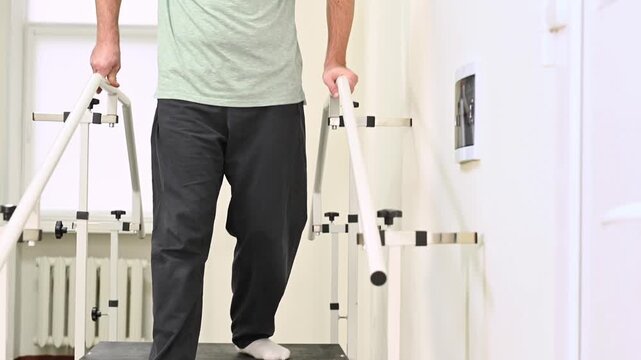 A man undergoes rehabilitation after an injury on a stair climber with parallel bars at a clinic under the supervision of a physical therapist. Close up legs on stairs