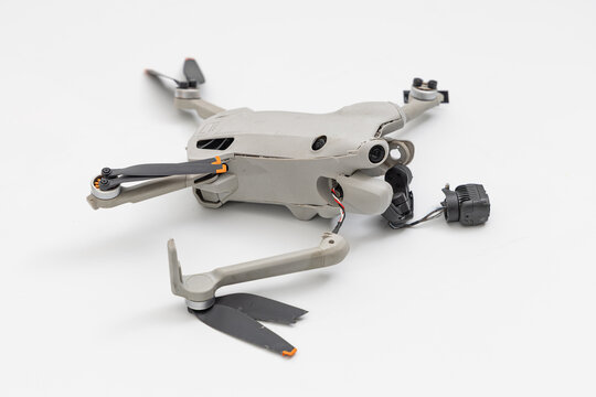 Broken modern drone after crash landing on white floor, damaged gimbal camera and snapped arm of quadcopter, electronics repair concept with selective focus on the cracked body.