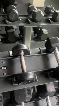 A pair of black dumbbells with the letters KG on the bottom. The dumbbells are on a rack