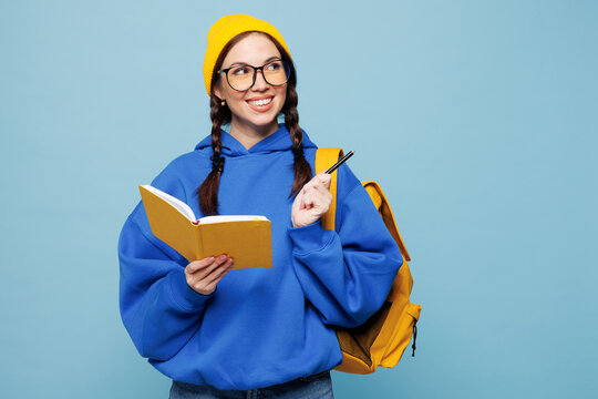 Young smart woman student she wear casual clothes yellow backpack bag hold write down in exercise book diary notes isolated on pastel plain light blue color background. High college lifestyle concept.