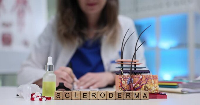 Wooden cubes spell word Scleroderma near layered skin model on table. Female rheumatologist writes notes tracking chronic autoimmune hardening signs