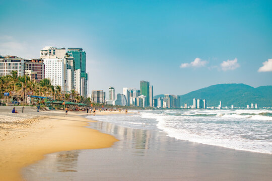 Danang beach in Vietnam with sea, distant mountains, high buildings and people walking along shore