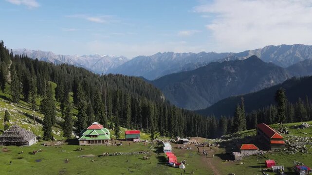 A lone kite in the sky with the background of mountains, huts and forest - 4K video, drone video, aerial shot, clip