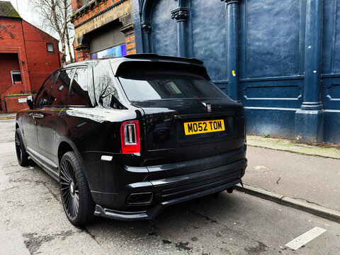 Black Rolls-Royce Cullinan SUV on a Manchester street with blue facade backdrop and UK license plate visible
