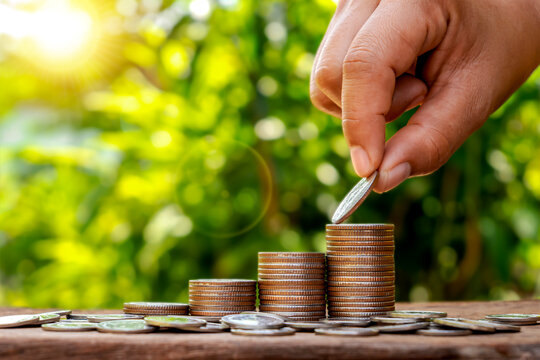 Close-up of a human hand placing a coin on a growing stack for financial growth and investment concept, business wealth management.