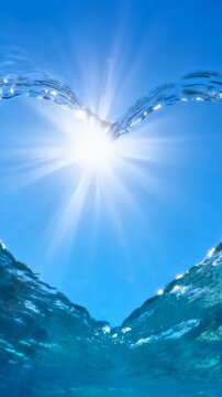 Vertical video: Rising swell lifting V-shaped cresting sea into split-level view, sun and sunbeams