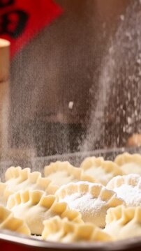 Vertical video: Falling powder dusting dumplings on metal tray in stall, steamers and red paper