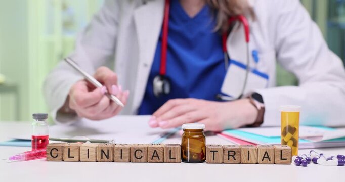 Wooden cubes spell phrase Clinical Trial near medical documents. Female doctor checks protocol writing notes for research study session in clinic