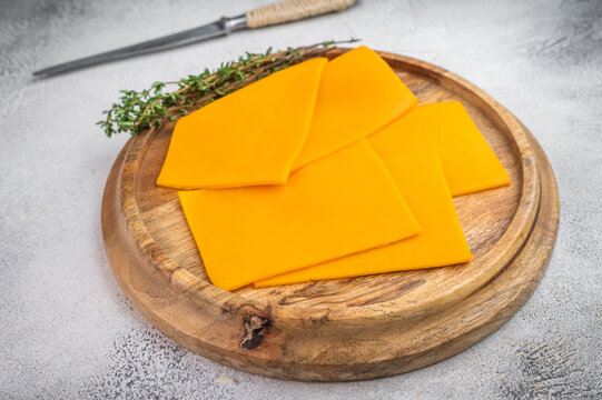 Cheddar cheese slices arranged on wooden plate with kitchen knife light concrete surface food background with copy space