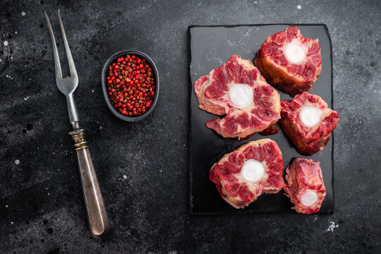 Butcher style raw oxtail pieces on dark slate board, traditional collagen rich meat for stock and slow cooking