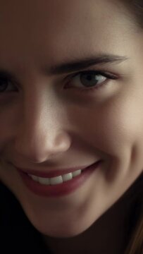Vertical video: Opening one eye, woman forming smile in soft-lit close-up, dimples and dark garment