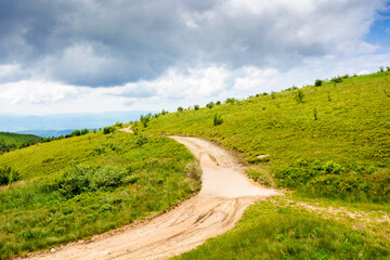 country dirt road through carpathian mountains of ukraine on a summer day. scenic view of green rolling hills under blue sky with clouds. beautiful alpine meadow and distant ridge for background