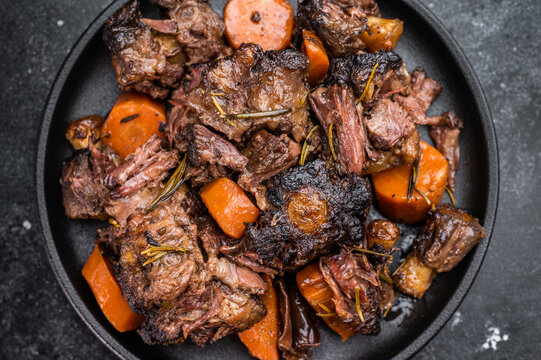 Slow cooked oxtails with vegetables and herbs, hearty comfort food served on dark background, top view