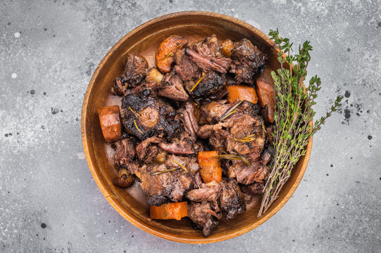 Braised veal oxtail stew with carrots and herbs served in wooden bowl, tender slow cooked meat in rich sauce