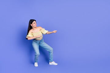 Obraz premium Young woman dancing in a purple studio background wearing yellow off the shoulder blouse blue jeans sneakers expressing joy and energy