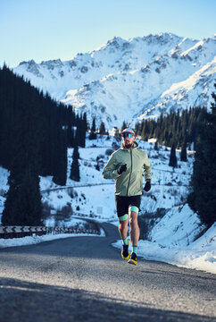 Man running on the road in the winter mountains