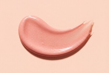 Fototapeta premium Top view of shimmering pink cosmetic cream smear isolated on a matching pastel peach background