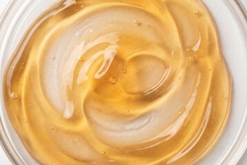 Swirled amber gold cosmetic gel texture with bubbles in a round glass container