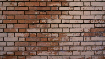 Obraz premium An old worn brick wall with bricks in different shades of red and beige