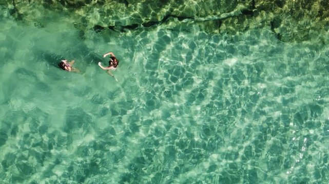 Aerial View of Two Women Swimming in Crystal Clear Turquoise Waters on a Sunny Summer Day at Sani Beach, Greece