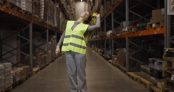 Warehouse worker adjusting helmet in storage facility with shelves full of products and boxes ready for distribution and shipment in an industrial logistics environment