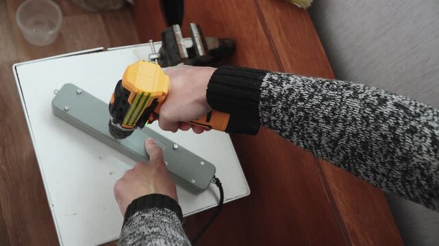Man screws lid of power strip with cordless screwdriver, top view. Master secures plastic cover of multi socket after repair in house.
