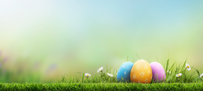 Three painted easter eggs celebrating a Happy Easter on a spring day with a green grass meadow, bright sunlight and a fresh spring background with copy space.