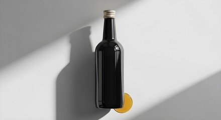 A black wine bottle with a gold cap on a white surface with a slice of orange