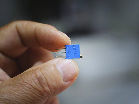 The image shows the trimmer potentiometer being clamped between the fingers of a technician.